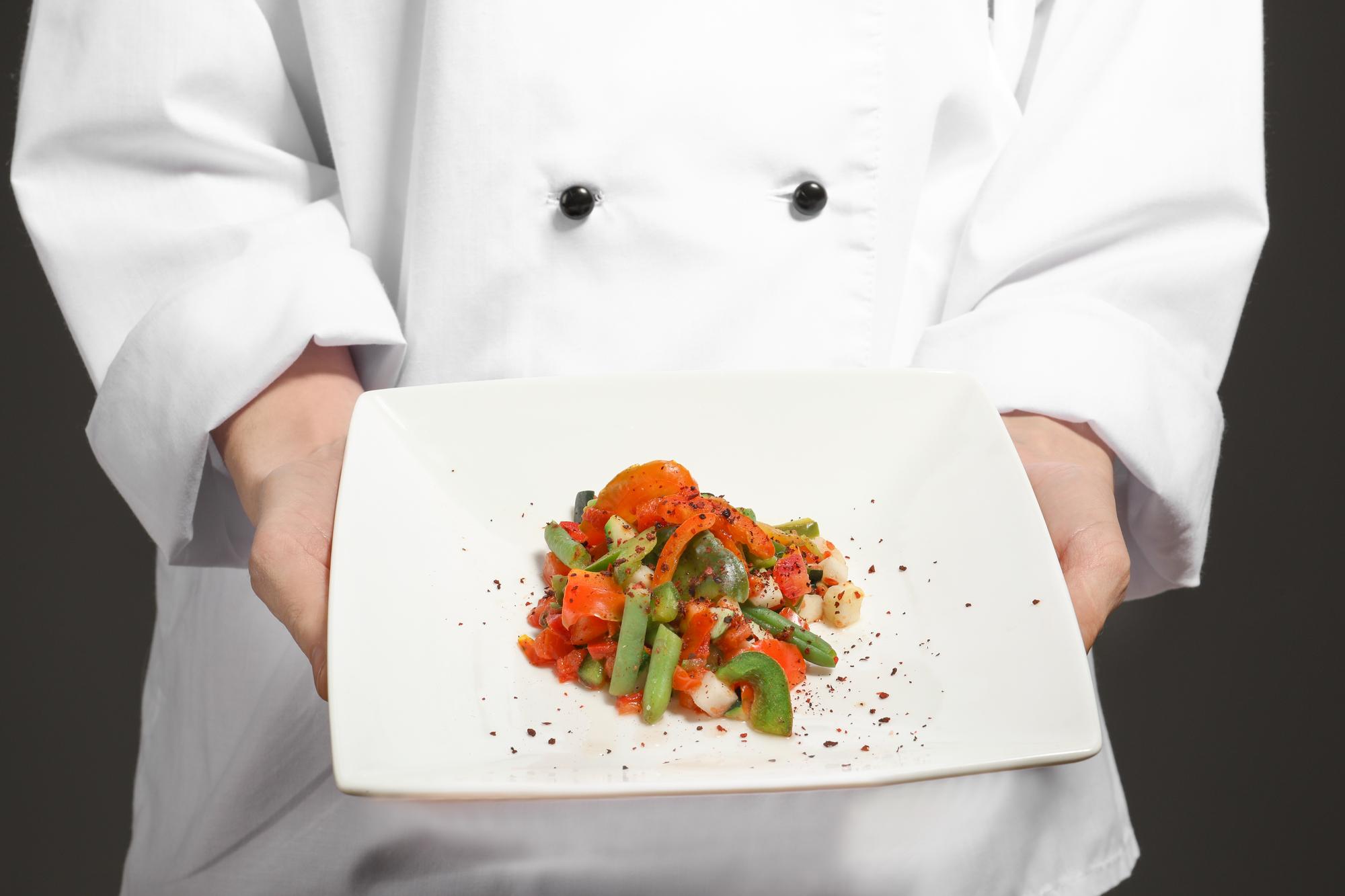 Chef demonstrating a plated dish in a calm kitchen